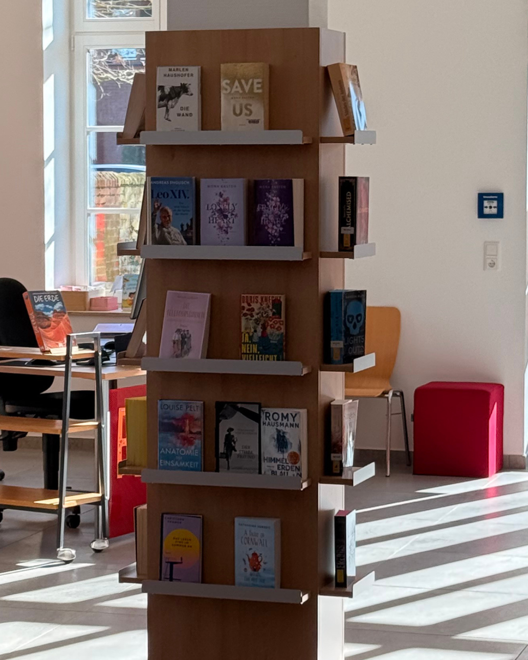 Blick auf eine Säule mit Büchern in der KÖB Steinfeld. Im Hintergrund ein Tisch für die Ausleihe.